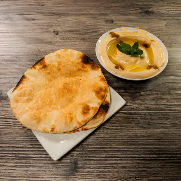 A bowl of Lebanese hummus drizzled with olive oil and mint, served with warm pita bread.