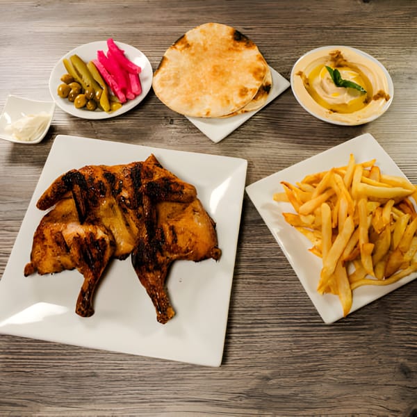 Lebanese grilled chicken, fries, hummus, pita bread, and pickled vegetables on a wooden table.