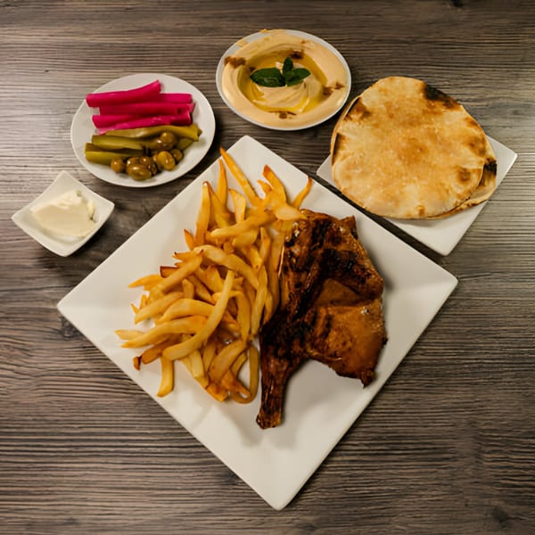 Lebanese grilled chicken with fries, hummus, pita bread, and pickled vegetables on a wooden table.